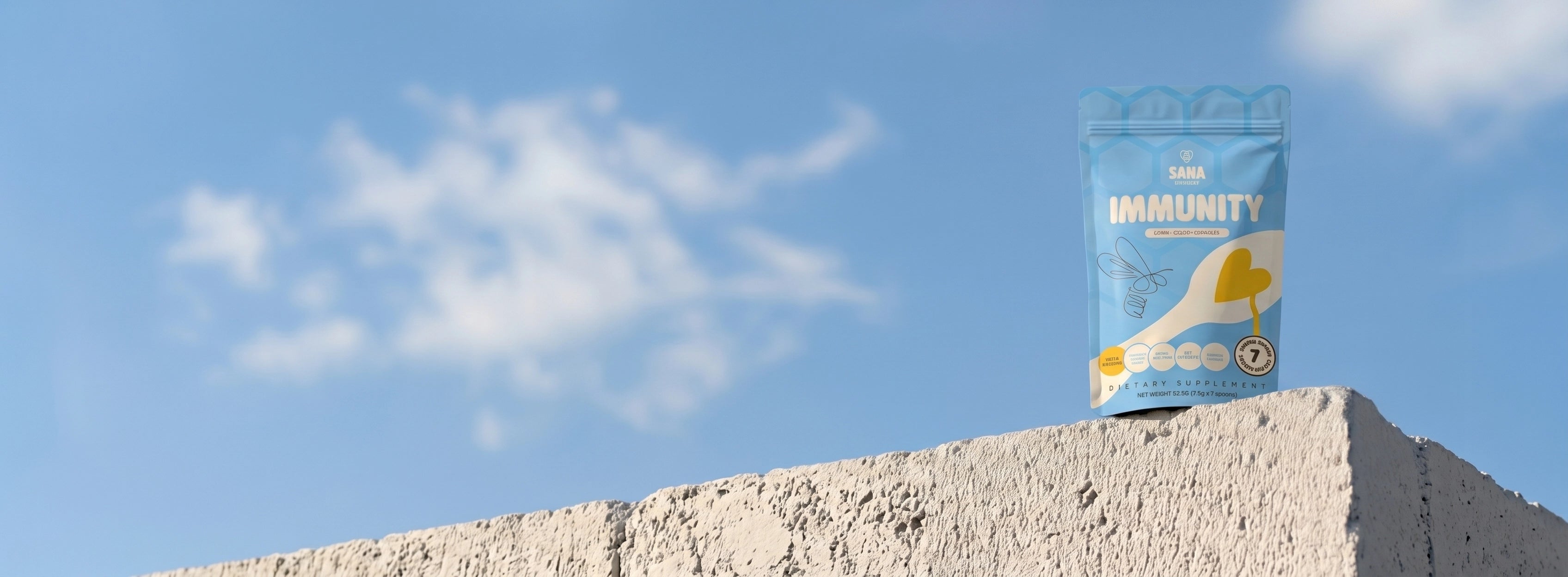 Sana VitaHoney Immunity Spoon package on a concrete ledge with a blue sky background.